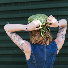 Load image into Gallery viewer, A woman ties a knot in a luxurious green scarf, tightening it at the back of her bob to keep her cool in the summer sun
